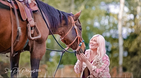 Woman petting a horse in an outdoor setting with blurred trees in the background