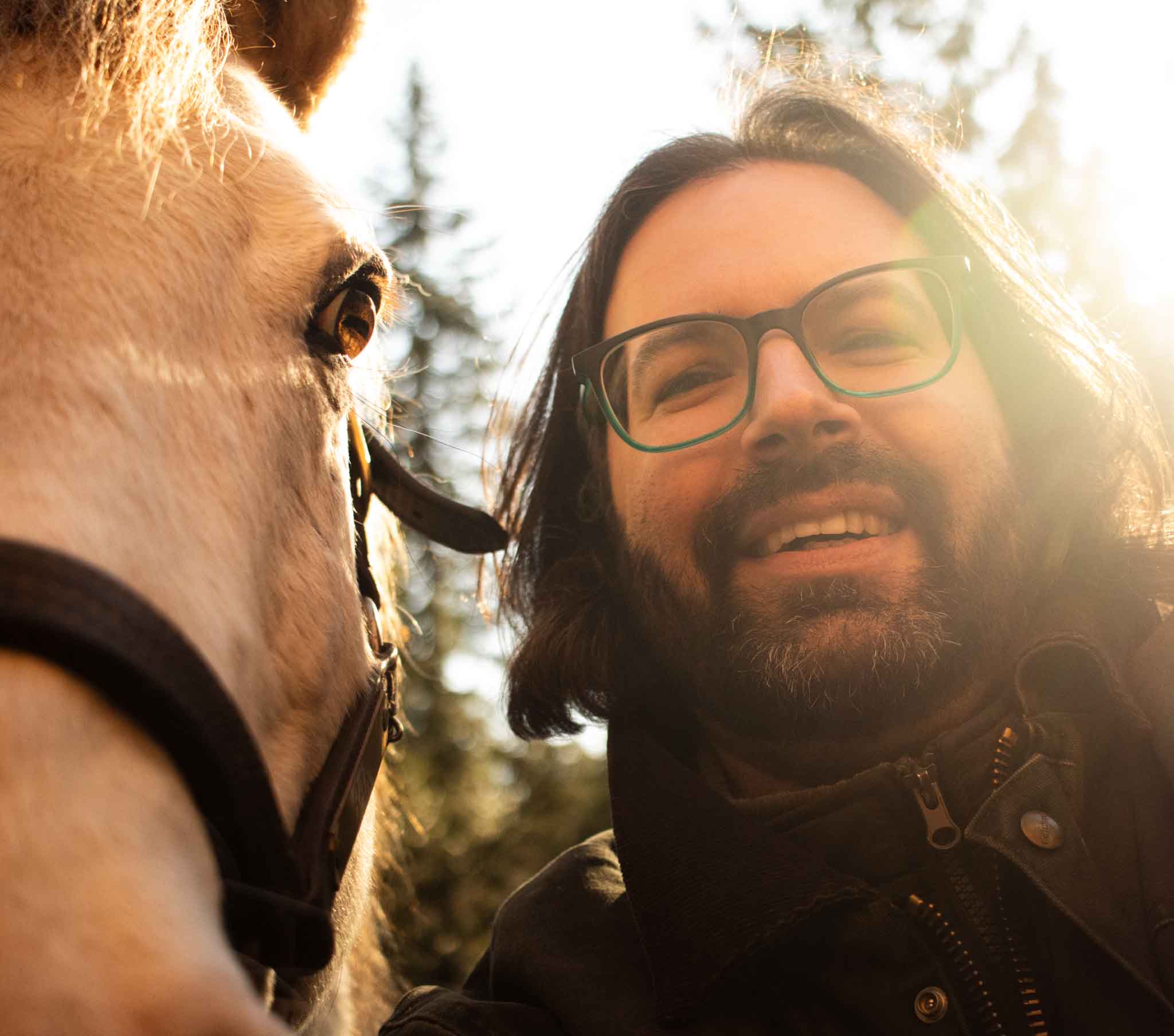 Man with glasses and beard smiling next to a horse outdoors